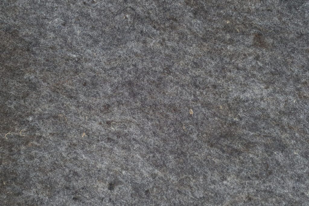 Close-up of a textured, dark gray stone surface with small fibers and particles