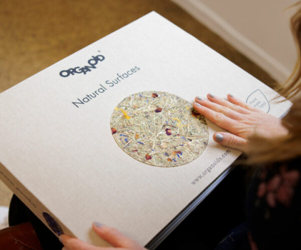 Hand resting on a book titled "Natural Surfaces" by Organoid GmbH with a circular image of text...
