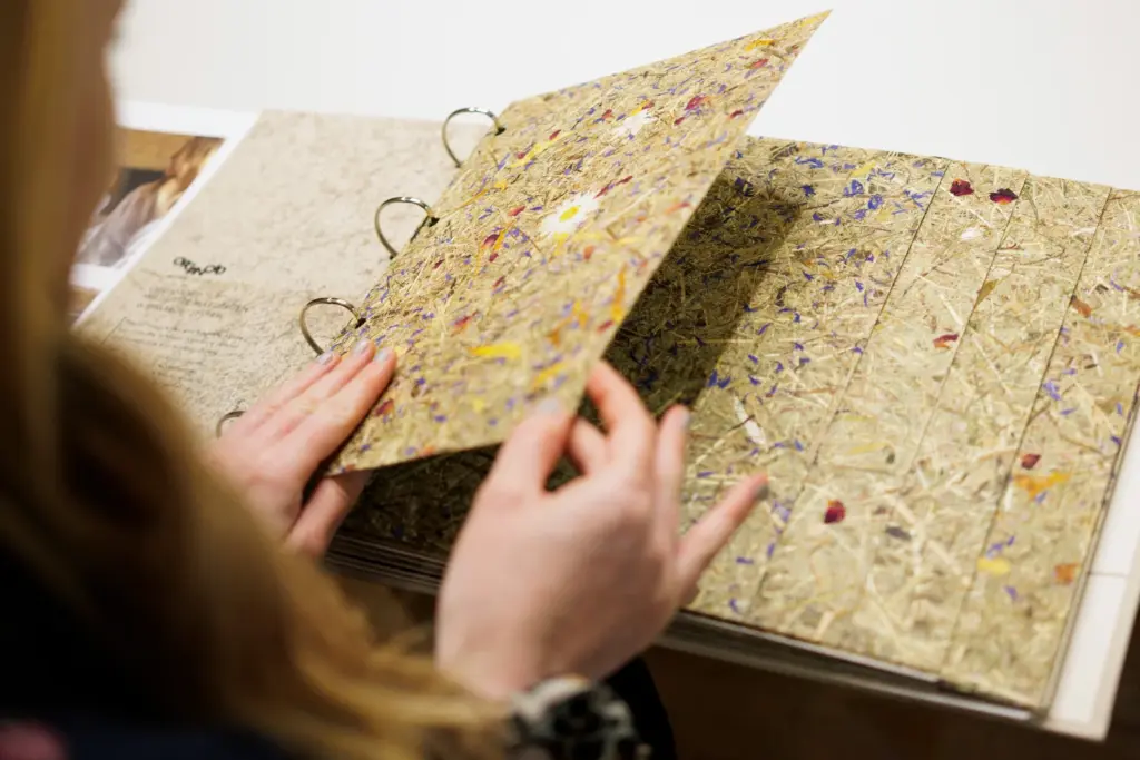 Person blätter in einem handgebundenen Buch mit bunten, getrockneten Blumen und Pflanzen.
