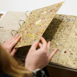 Person blätter in einem handgebundenen Buch mit bunten, getrockneten Blumen und Pflanzen.