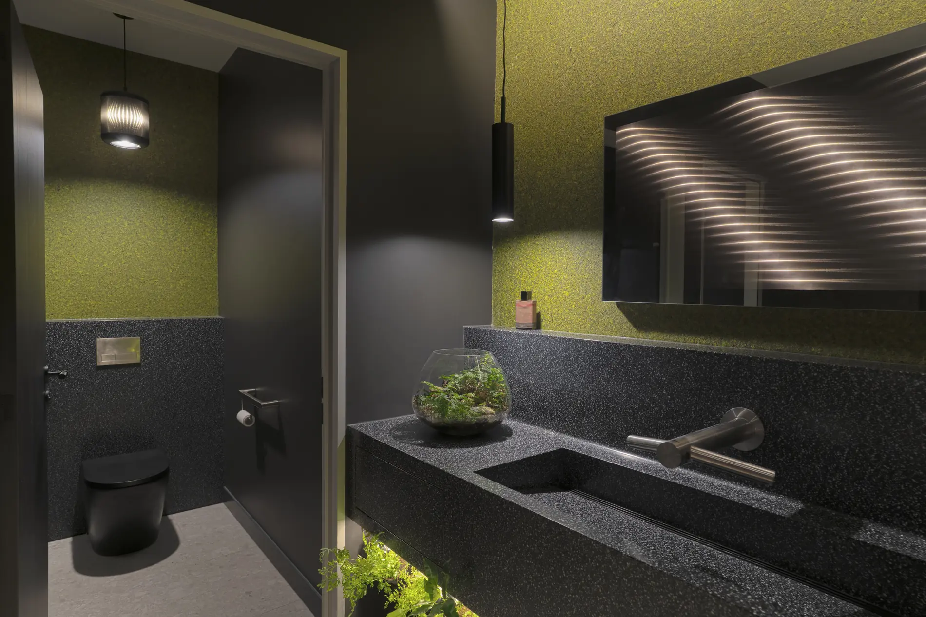 Moderner Badezimmerraum mit schwarzer Toilette, grüner Wand aus echtem Moos von Organoid und Wasserpflanzen auf der Ablage. Biophiles Design