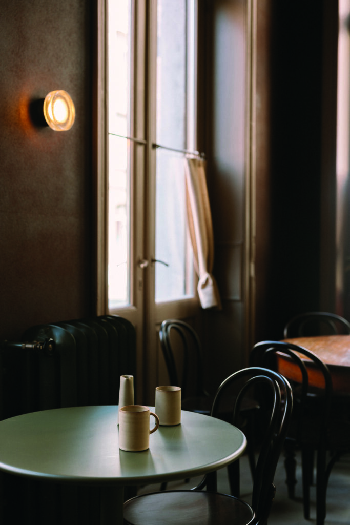 Ein ruhiger Raum mit einem runden Tisch, drei Keramikbechern und einem Fenster mit Vorhängen