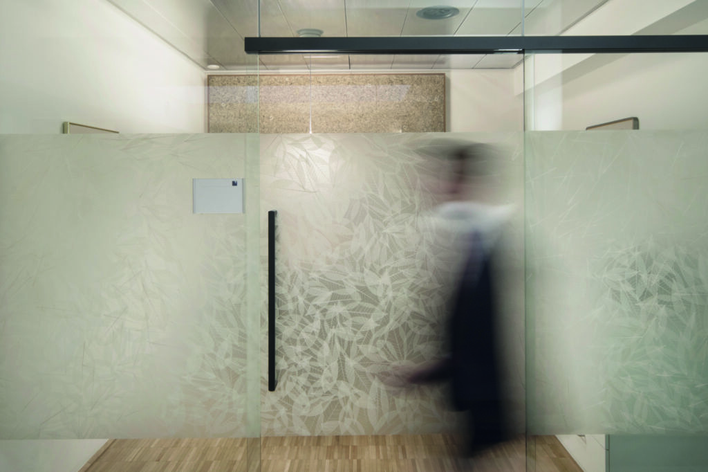 Blurry person walking past frosted glass door with leaf pattern in an office hallway