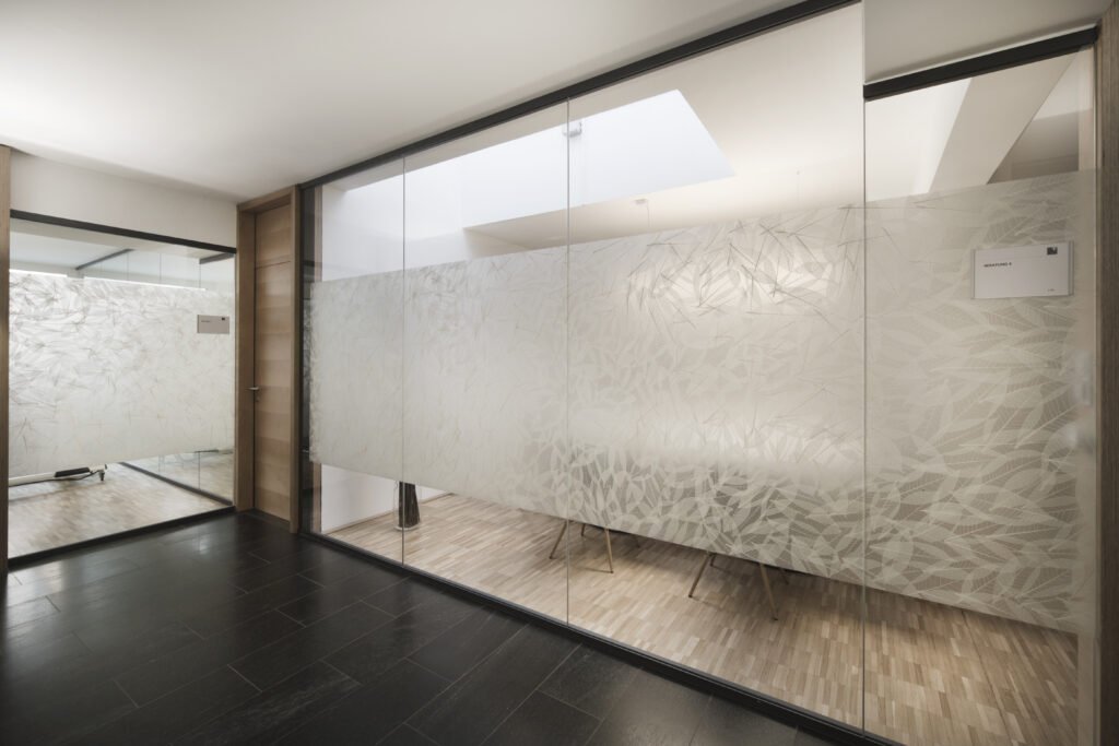 Glass partition with frosted leaf pattern dividing a modern office space with skylight and wood...