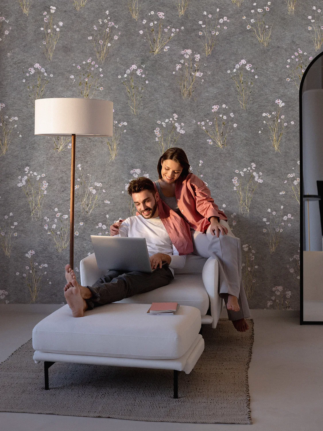 Zwei lachende Menschen sitzen auf einem weißen Sofa, schauen gemeinsam auf einen Laptop.