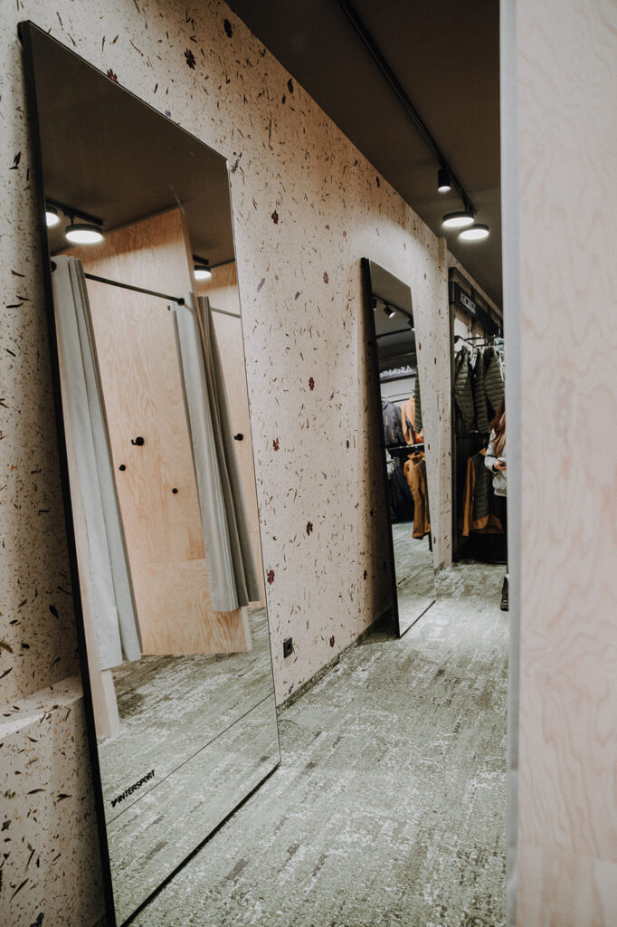 Full-length mirror reflecting a fitting room with curtains and clothing racks in a retail store