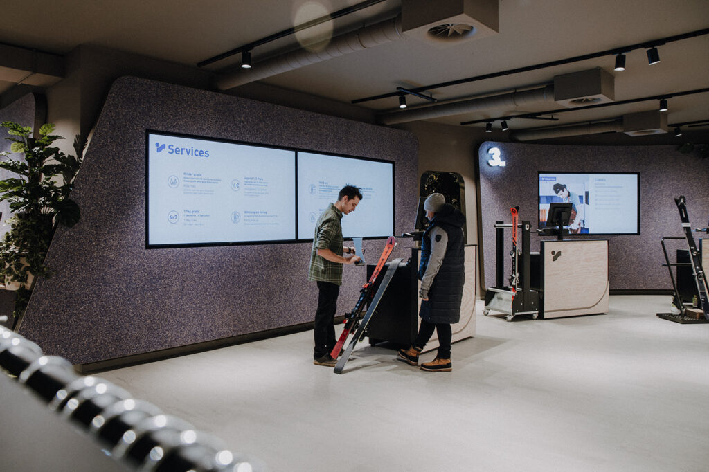 Two people at a service desk in a modern, well-lit indoor space with digital screens behind them