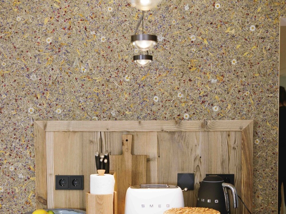 Küchenbereich mit Holzrückwand, Kaffeemaschine, Toaster, Teekanne und Obst, vor einer bunten Wand