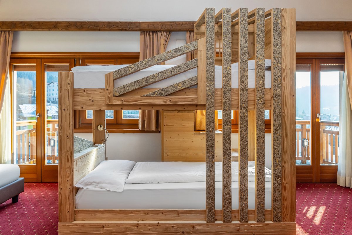 Ein Holzhochbett mit schrägen Steinverkleidungen vor großen Fenstern in einem Zimmer