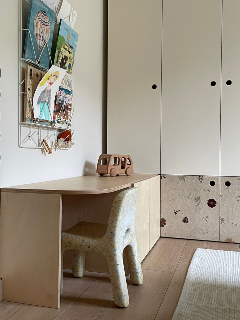 Kinderarbeitsbereich mit Holzschreibtisch, Stuhl, Spielzeugbus und Wandmagazin in einem Kinderzimmer