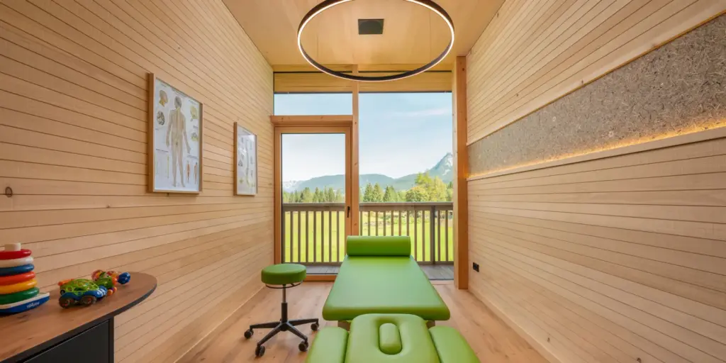 Physiotherapieraum mit ORGANOID Naturoberfläche und grüner Liege vor Bergkulisse