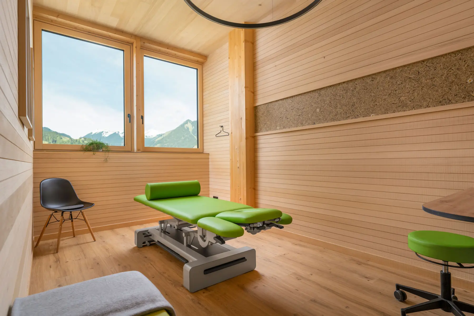 Physiotherapieraum mit ORGANOID Naturoberfläche und grüner Liege vor Bergkulisse