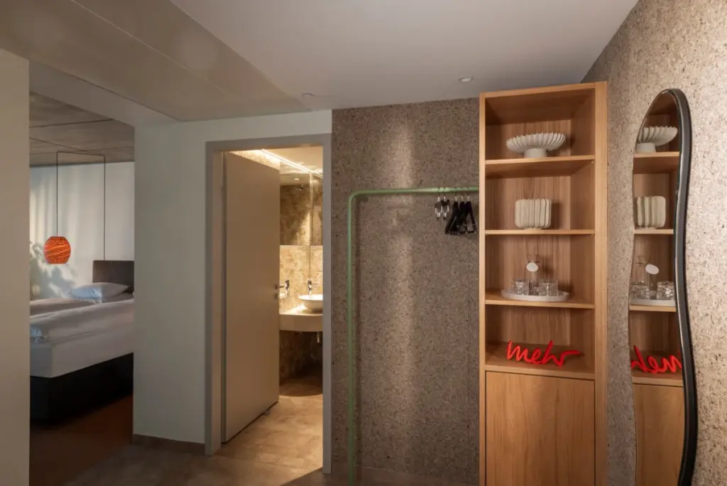 Hotelzimmer-Eingang mit Wandverkleidung aus ORGANOID Moos Grau, daneben ein Eichenregal und ein Wellenspiegel